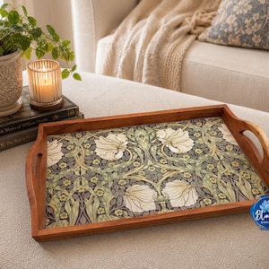May include: A rectangular wooden serving tray featuring a decorative floral pattern with white flowers, green leaves, and yellow accents on a dark background. The tray has integrated side handles and a smooth, polished finish on the wooden frame.