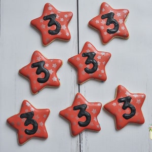 May include: Seven red star-shaped sugar cookies decorated with silver glitter and a black number "3" on each cookie.