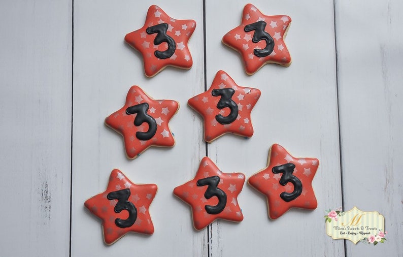 May include: Seven red star-shaped sugar cookies decorated with silver glitter and a black number "3" on each cookie.