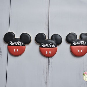 May include: Three red and black Mickey Mouse-shaped cookies with white icing and the name "DAVID" written on each cookie.