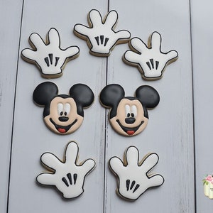May include: A set of eight Mickey Mouse themed cookies. There are two cookies with Mickey Mouse's face, and six cookies shaped like Mickey Mouse's white gloves.