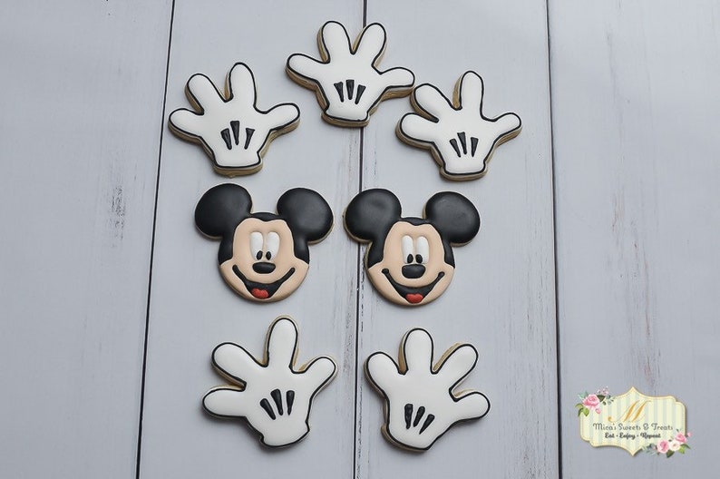 May include: A set of eight Mickey Mouse themed cookies. There are two cookies with Mickey Mouse's face, and six cookies shaped like Mickey Mouse's white gloves.