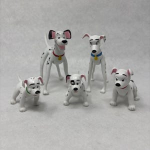May include: A set of five plastic Dalmatian dog figurines. One large adult dog with a red collar, one adult dog with a blue collar, and three smaller puppies with green, red, and no collars. Each figure features black spots and white bodies.