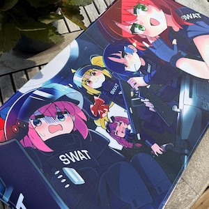 Puede incluir: Una alfombrilla de ratón rectangular con una colorida ilustración de estilo anime de varios personajes con uniformes SWAT. Los personajes tienen el pelo de colores brillantes y están sobre un fondo azul oscuro. La palabra "SWAT" es visible en los uniformes.