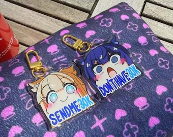 Puede incluir: Dos llaveros de estilo anime con cierres dorados. Un llavero presenta un personaje con cabello naranja y el texto "SEND ME 30K". El otro llavero tiene un personaje de cabello azul y el texto "DON'T HAVE 30K". Descansan sobre una superficie azul oscuro estampada.