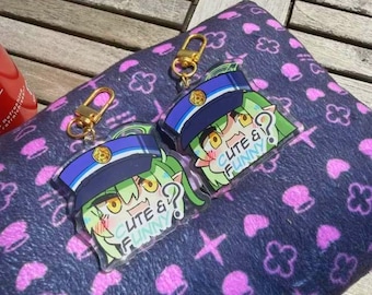Puede incluir: Dos llaveros acrílicos con un personaje de dibujos animados con pelo verde y gorra de policía. Los llaveros tienen cierres dorados y el texto "CUTE & FUNNY". Están sobre una superficie estampada azul oscuro.