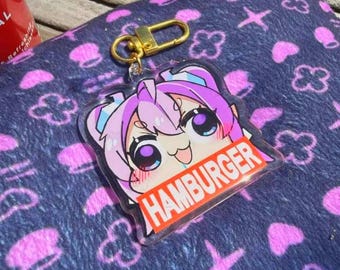 Puede incluir: Un llavero acrílico transparente con un personaje de anime de pelo rosa y ojos grandes. El llavero tiene un cierre dorado y la palabra "HAMBURGER" en un rectángulo rojo.