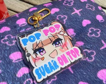 Puede incluir: Un llavero acrílico transparente con un diseño de personaje de estilo anime. El llavero presenta el texto "POP POP SUGAR ON TOP" en azul y rosa. Tiene un cierre de color dorado.