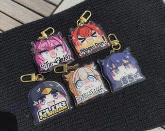 Puede incluir: Una colección de llaveros de estilo anime con cierres dorados. Cada llavero presenta un diseño de personaje único con colores vibrantes y texto, incluyendo "The Cake", "Häagen-Dazs", "CLUB PENGUIN", "DONT LAY EGGS" y "85 INT".