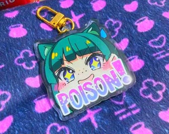 Puede incluir: Un llavero acrílico transparente con un personaje de estilo anime con cabello verde azulado y la palabra "POISON!" en una fuente colorida. El llavero tiene un cierre dorado, sobre un fondo azul estampado.