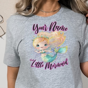 May include: Gray t-shirt with a cartoon mermaid illustration and the text "Your Name the Little Mermaid".