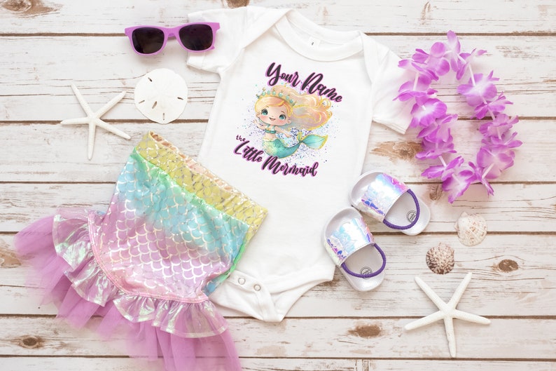 May include: A white bodysuit with a mermaid illustration and the text "Your Name the Little Mermaid". The bodysuit is paired with a rainbow iridescent mermaid tail skirt, purple flower lei, and white starfish.