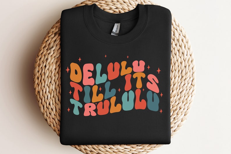 Puede incluir: Sudadera negra con un gr&aacute;fico colorido que dice "Delulu Till It's Trululu" en una fuente retro.