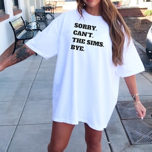 May include: White oversized t-shirt with black text that reads "Sorry. Can't. The Sims. Bye."