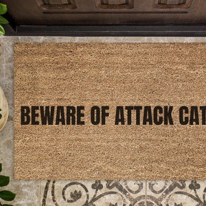 May include: A brown coir doormat with the text "BEWARE OF ATTACK CAT." printed in black.