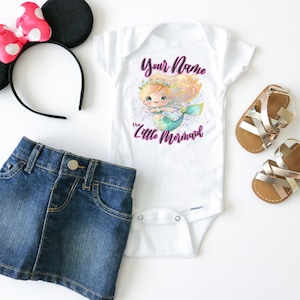 May include: A white bodysuit with a mermaid illustration and the text "Your Name the Little Mermaid". The bodysuit is paired with a denim skirt, a pair of gold sandals, and a black headband with a pink bow.