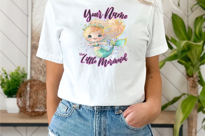 May include: White t-shirt with a cartoon mermaid wearing a crown and the text "Your Name the Little Mermaid" in purple.