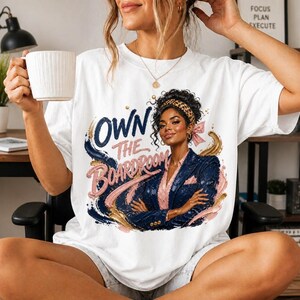 Può includere: Una t-shirt bianca con un'illustrazione grafica di una persona con capelli scuri ricci, una fascia leopardata e un blazer blu navy. Il testo OWN THE BOARDROOM è scritto in grassetto corsivo blu navy e rosa con accenti color oro.