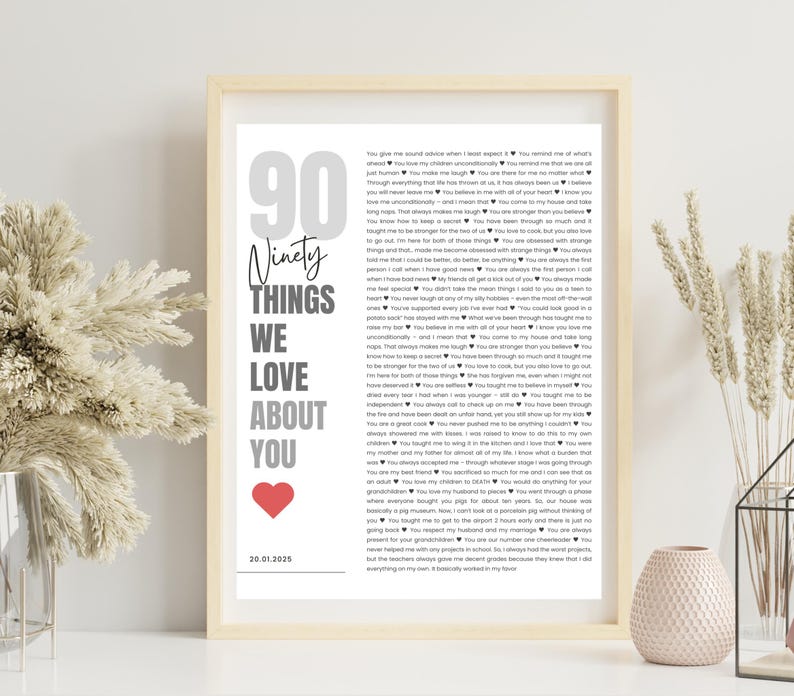 May include: A framed print with the text "90 Things We Love About You" in gray and black, with a red heart. The print includes a list of loving sentiments and a date at the bottom. The frame is a light wood color.