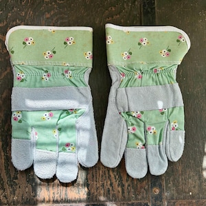 May include: A pair of green gardening gloves with a floral print and grey leather palms.