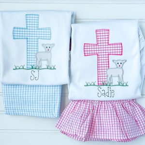 K&ouml;nnte beinhalten: Zwei wei&szlig;e Hemden mit gestickten Kreuzen und L&auml;mmern. Das Hemd links hat ein blaues Kreuz und den Text "SJ". Das Hemd rechts hat ein pinkfarbenes Kreuz und den Text "Sadie".