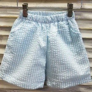 May include: Light blue shorts with a white and light blue striped pattern. The shorts have an elastic waistband and a drawstring.