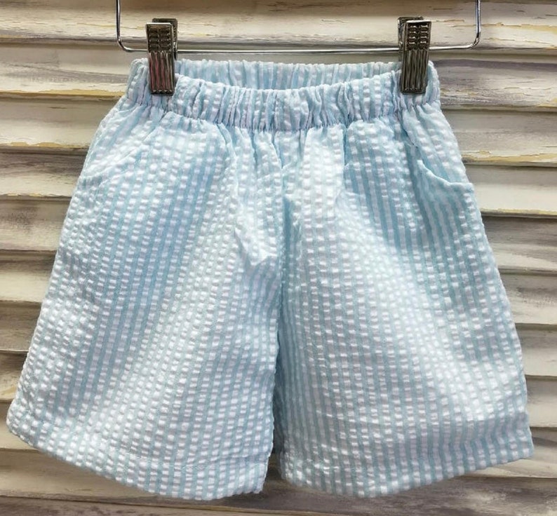 May include: Light blue shorts with a white and light blue striped pattern. The shorts have an elastic waistband and a drawstring.