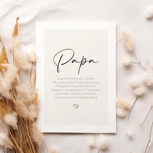 May include: A framed print with the word "Papa" in elegant script. Below, a list of qualities such as "Super Hero" and "Motivator" are listed. The print is surrounded by dried beige ornamental grasses.