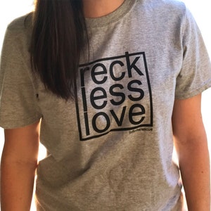 May include: Gray t-shirt with the words "reckless love" in a black box. The words are stacked vertically. The text "infiniterescue" is below the box.