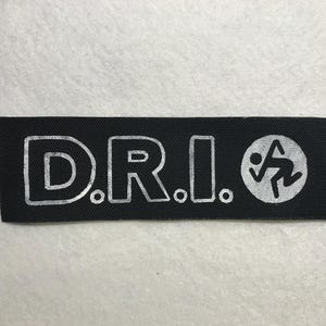 Könnte beinhalten: Schwarzer rechteckiger Aufnäher mit den silbernen Buchstaben "D.R.I." und einer kreisförmigen Grafik einer laufenden Figur. Der Aufnäher ist wahrscheinlich für Kleidung oder Accessoires.