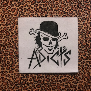 May include: Black and white iron-on patch featuring a skull wearing a bowler hat and crossed bones. The text "ADDICTS" is below the skull.