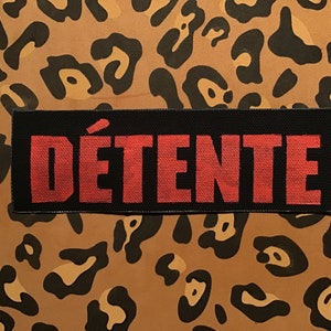 May include: A black fabric patch with the word "DÉTENTE" in red lettering.