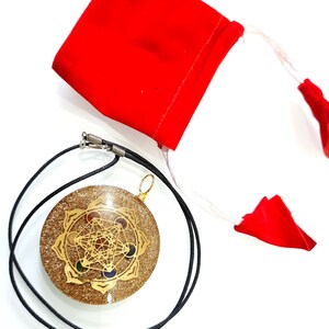 May include: A gold-colored pendant with a geometric design and colorful stones, on a black cord, with a red velvet pouch.