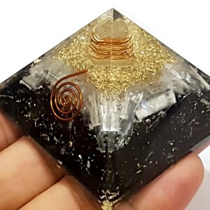 May include: Black, white, and gold crystal pyramid with a copper wire spiral inside. The pyramid is made of layered crystals and is a popular item for meditation and energy work.