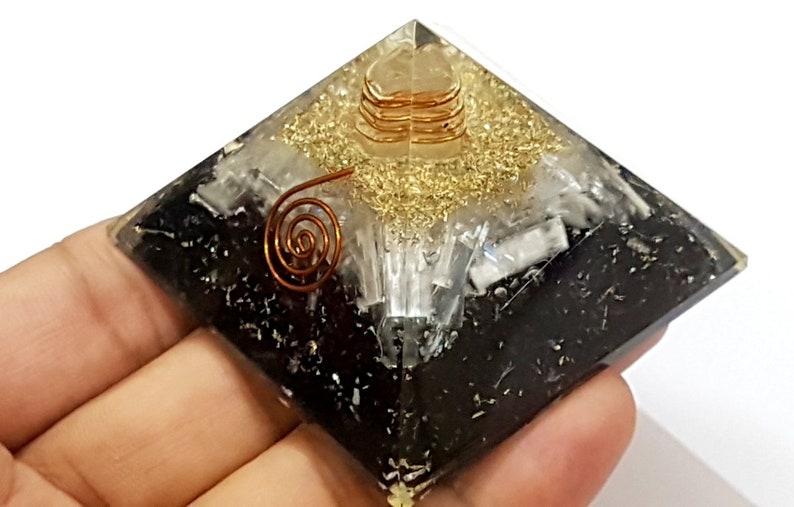 May include: Black, white, and gold crystal pyramid with a copper wire spiral inside. The pyramid is made of layered crystals and is a popular item for meditation and energy work.