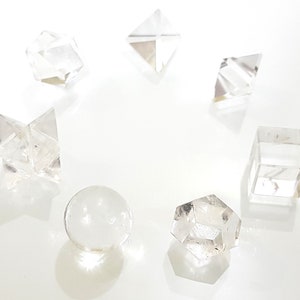 Könnte beinhalten: Ein Set aus sieben klaren Quarzkristallformen, darunter eine Kugel, ein Würfel, eine Pyramide, ein Stern und drei weitere geometrische Formen.