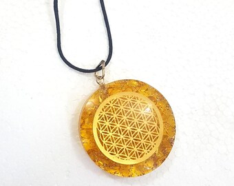Può includere: Una collana con un ciondolo dorato su un cordoncino nero. Il ciondolo ha un design circolare con un motivo a fiore della vita.