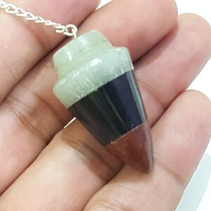May include: A three-toned crystal pendulum with a silver chain. The top of the pendulum is light green, the middle is black, and the bottom is reddish-brown.