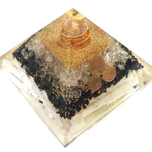 Puede incluir: Una pirámide de cristal transparente con capas de cristales negros, blancos y dorados. La pirámide tiene espirales de alambre de cobre en la parte superior y en el interior.