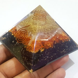 May include: A handcrafted pyramid-shaped resin art piece. The pyramid features layers of black, orange, and gold elements, with copper wire spirals and coils embedded within. The pyramid is approximately 3 inches square.