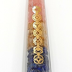 May include: A clear quartz crystal point with seven chakra stones and gold symbols inside. The stones are pink, orange, yellow, green, blue, indigo, and violet. The symbols are the chakras symbols.