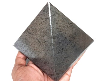 May include: A dark gray pyramid-shaped crystal with a white line running down the center.