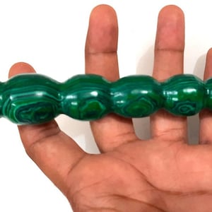 Puede incluir: Una varita de cristal de malaquita verde con una punta puntiaguda y una serie de protuberancias redondeadas a lo largo del eje.