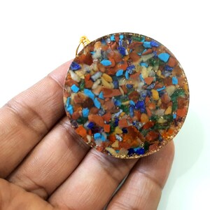 May include: A round, multi-colored pendant with a gold wire loop. The pendant is made of resin and contains small pieces of various gemstones, including turquoise, lapis lazuli, carnelian, and jasper.