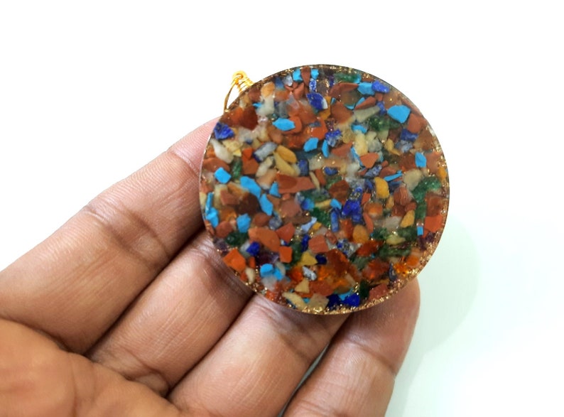 May include: A round, multi-colored pendant with a gold wire loop. The pendant is made of resin and contains small pieces of various gemstones, including turquoise, lapis lazuli, carnelian, and jasper.