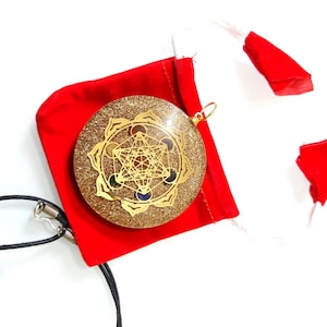 May include: A gold-colored pendant with a geometric design and colorful stones, set in a clear resin base with glitter. The pendant is on a black cord and comes in a red velvet pouch.