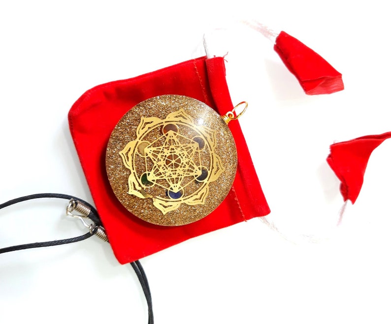 May include: A gold-colored pendant with a geometric design and colorful stones, set in a clear resin base with glitter. The pendant is on a black cord and comes in a red velvet pouch.