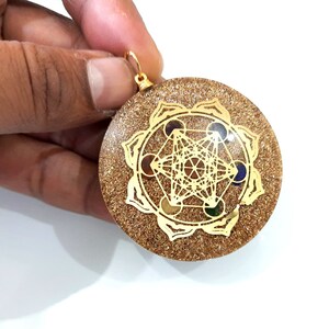 May include: Gold-toned pendant with a geometric design and colorful stones. The pendant is round and has a sparkly, glittery surface.