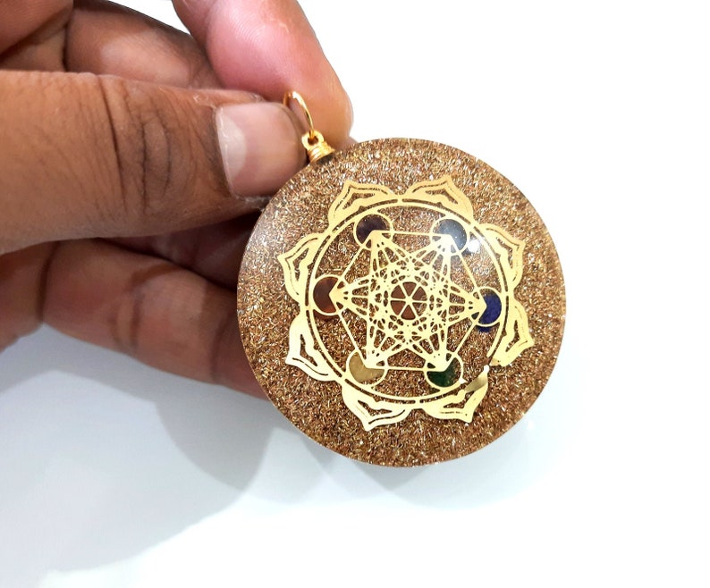 May include: Gold-toned pendant with a geometric design and colorful stones. The pendant is round and has a sparkly, glittery surface.