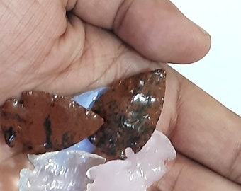 Puede incluir: Cuatro puntas de flecha hechas de diferentes tipos de piedra. Dos son marrones y negras, una es azul claro y una es rosa.